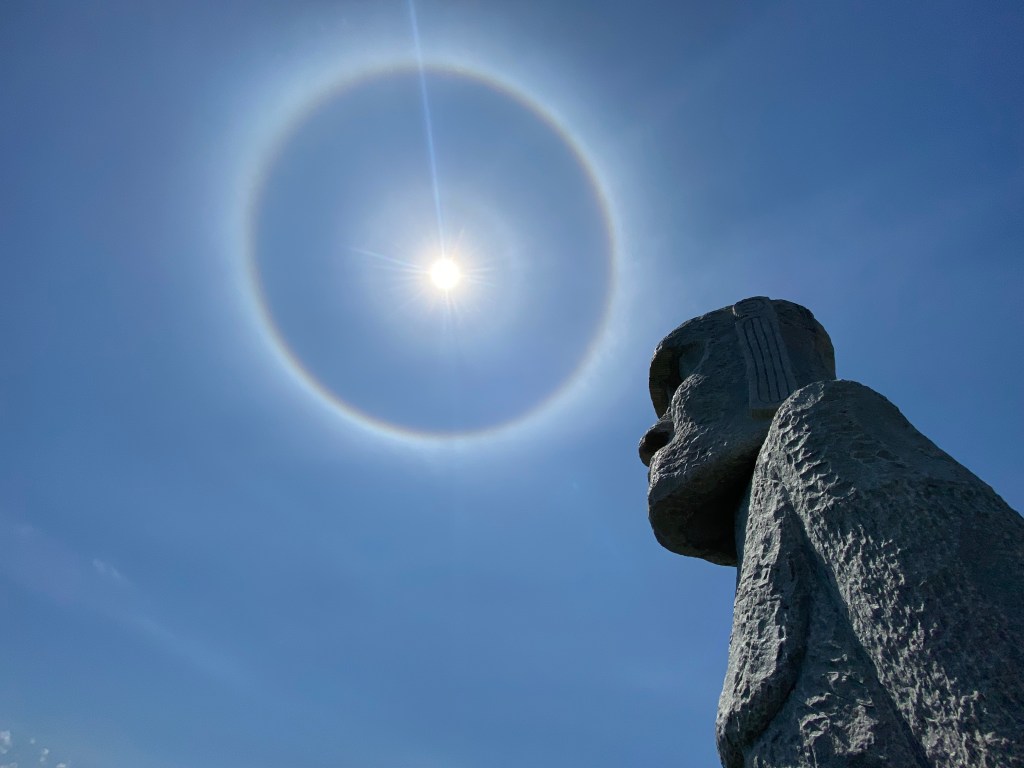 A solemn Moai statue gazes skyward beneath a 22-degree halo—Makomanai Takino Cemetery, Sapporo, Japan.